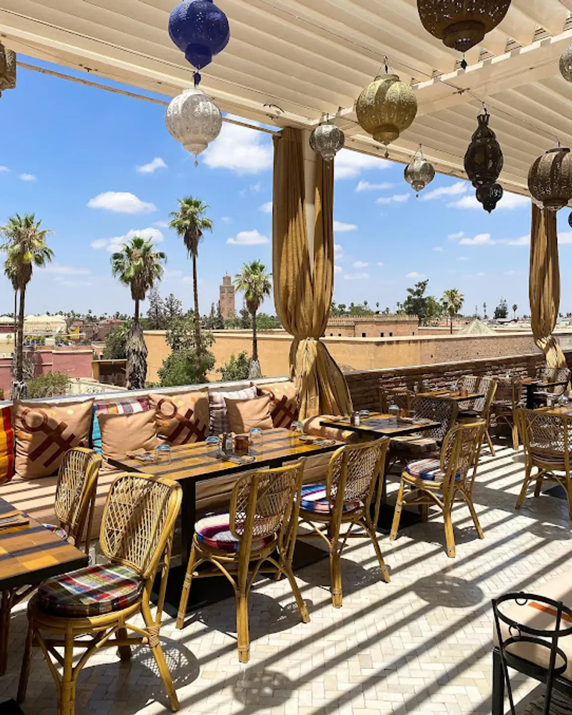 Rooftop terrace at DarDar Rooftop in Marrakech, with city views, palm trees, and lanterns.