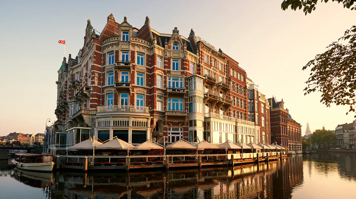 De L’Europe Amsterdam hotel exterior with canal view in Amsterdam at sunset.