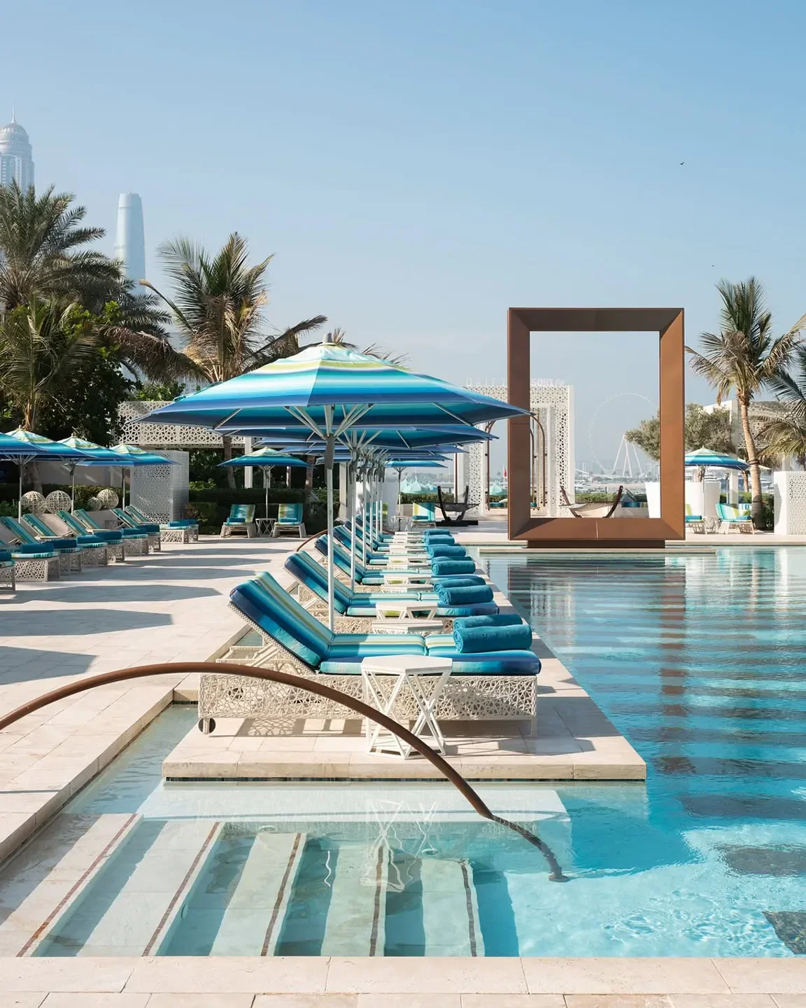 Luxury pool area at DRIFT Beach Dubai with sun loungers and blue umbrellas.