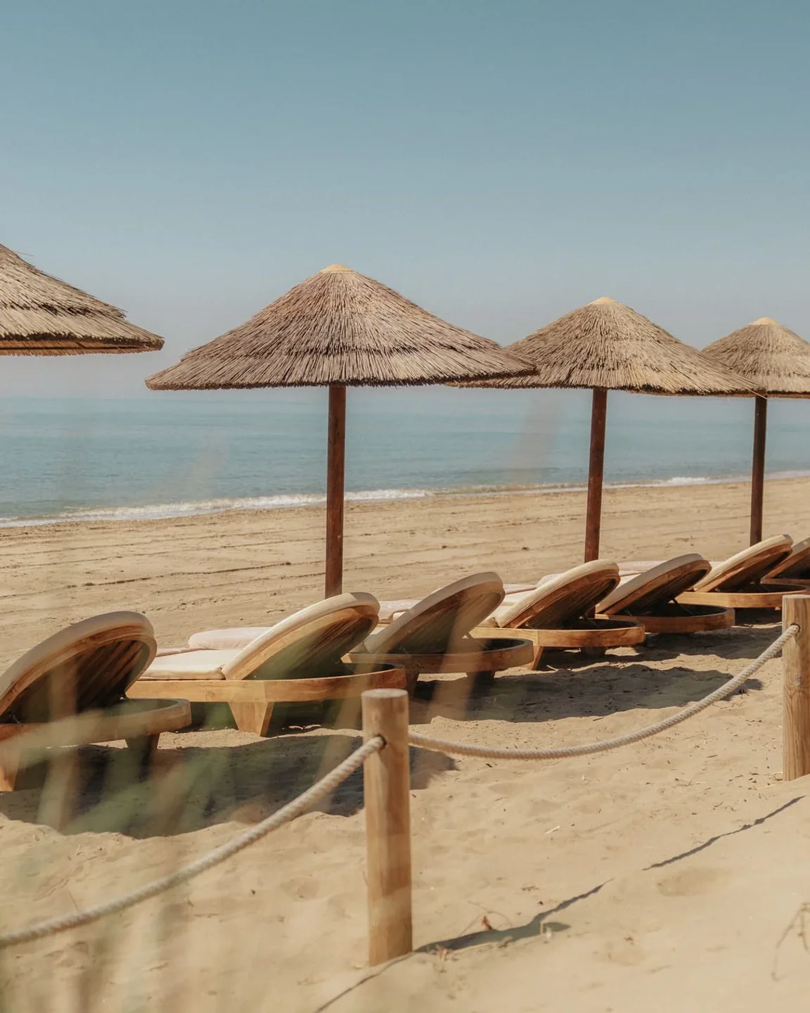 Dune Beach Marbella: empty lounge chairs and thatched umbrellas on sandy beach with ocean view.