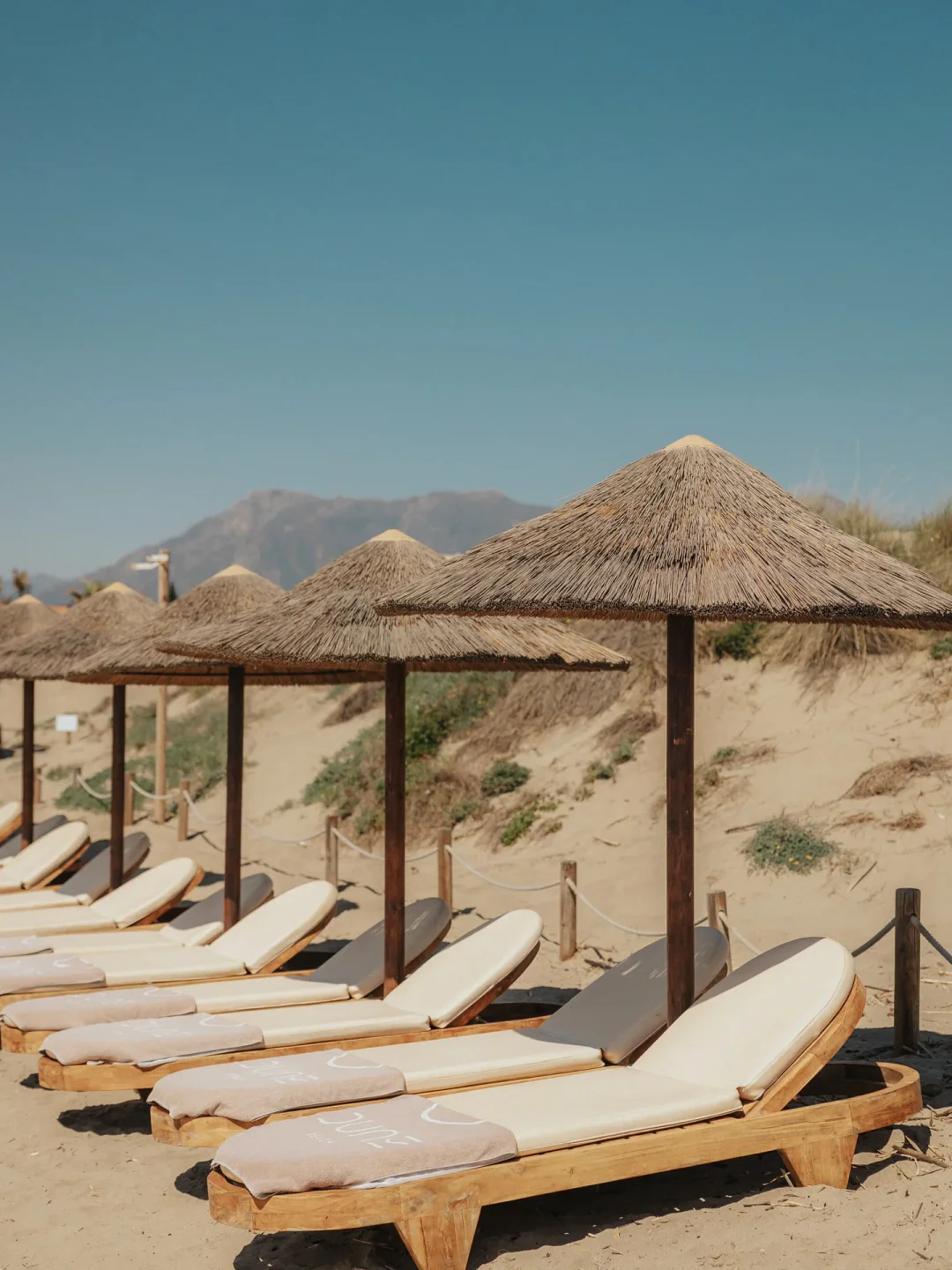 Row of sun loungers and thatched umbrellas at Dune Beach, Marbella, ready for guests on a sunny day.