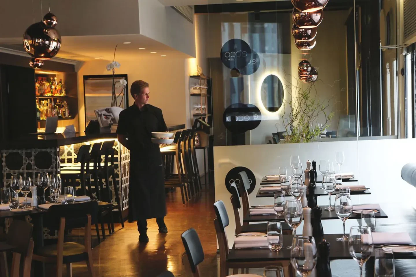 Elegant dining room interior at E'cco Bistro in Brisbane with a waiter serving.