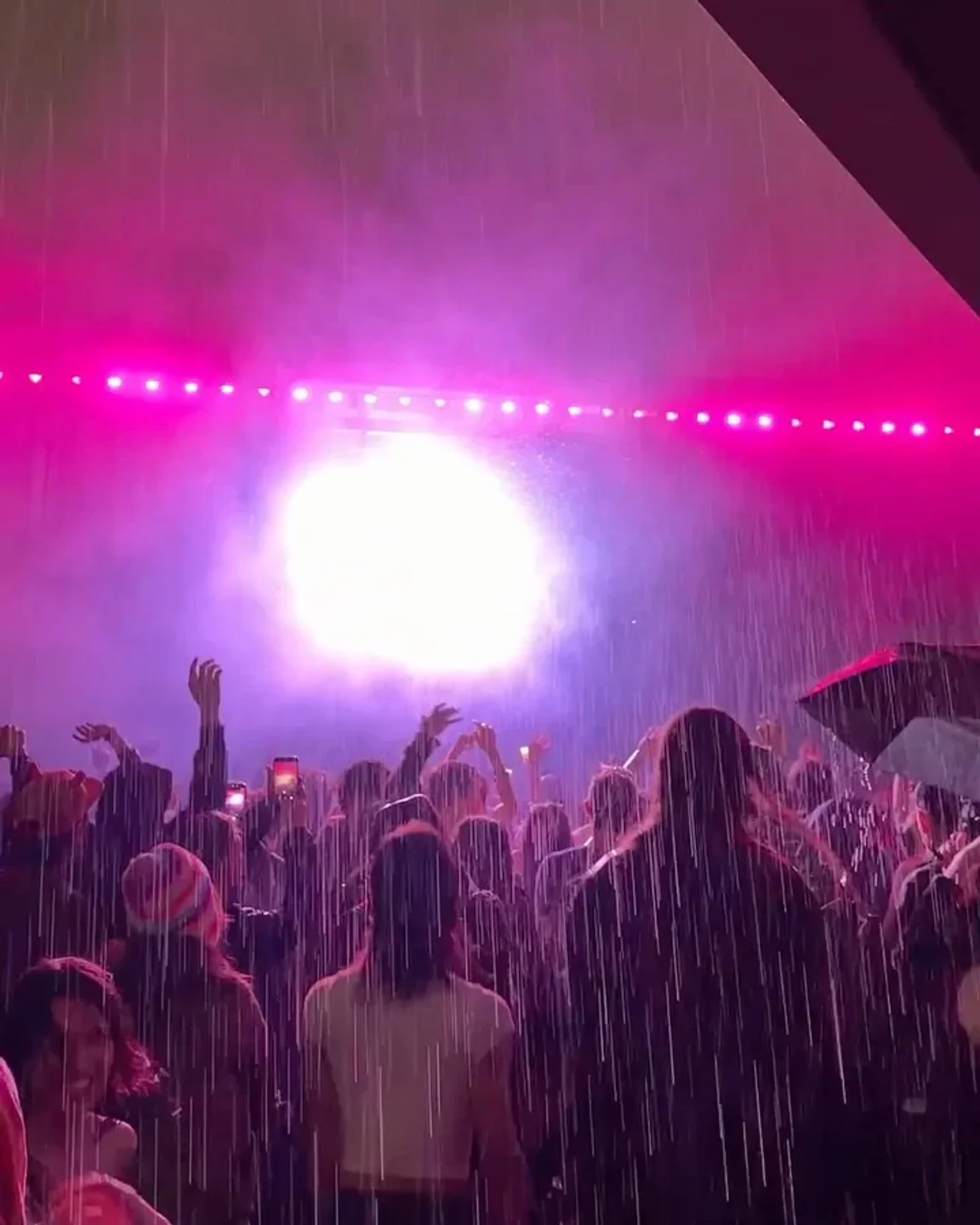 Crowd dancing in the rain at Elsewhere nightclub under vibrant pink lights and stage fog.