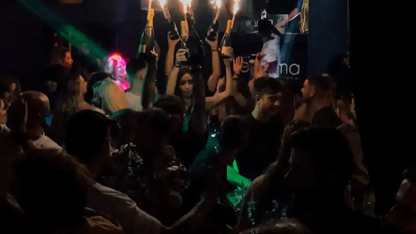 Energetic crowd celebrating at Enigma Club in Santorini with champagne bottles held high