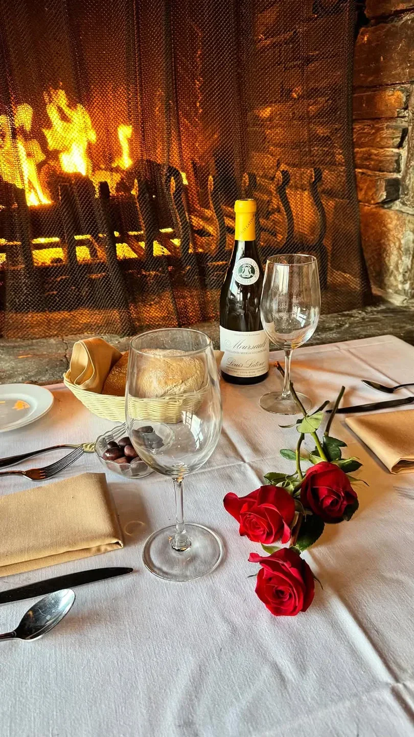 Cozy table setting at Fandango Restaurant in Carmel with fireplace, wine, roses, and bread.