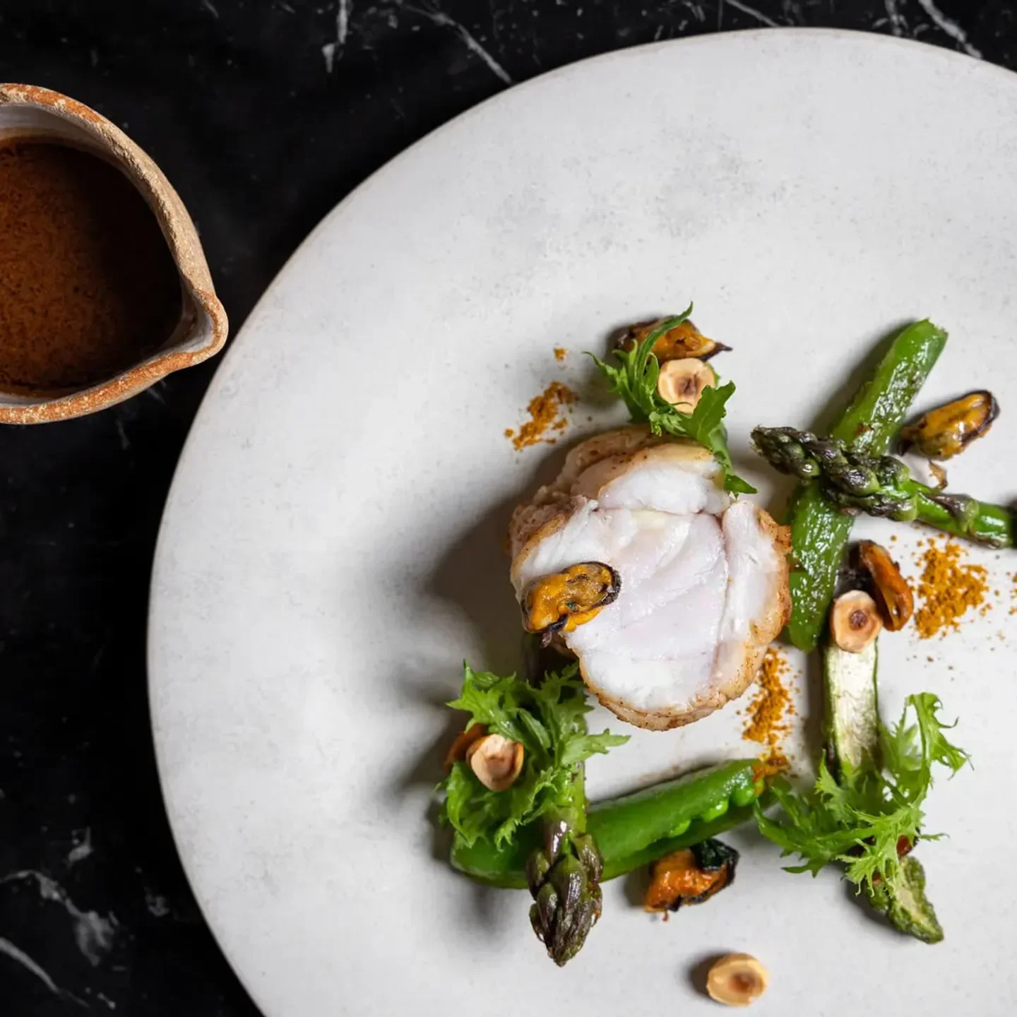 Delicious dish from Fleur de Pavé, Paris. Grilled fish with asparagus and mussels on a plate.