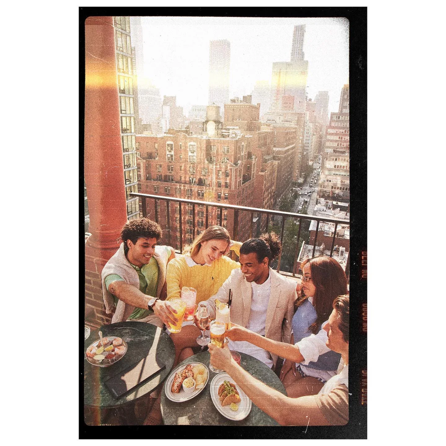 Friends enjoying drinks and appetizers at FREEHOLD Rooftop in New York City with a city skyline view.