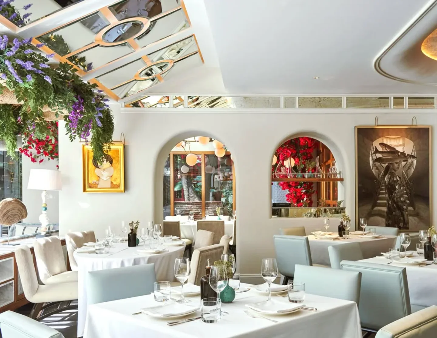 Elegant dining room at GAIA restaurant in Marbella, featuring white tablecloths, plush seating, and artistic wall decor.