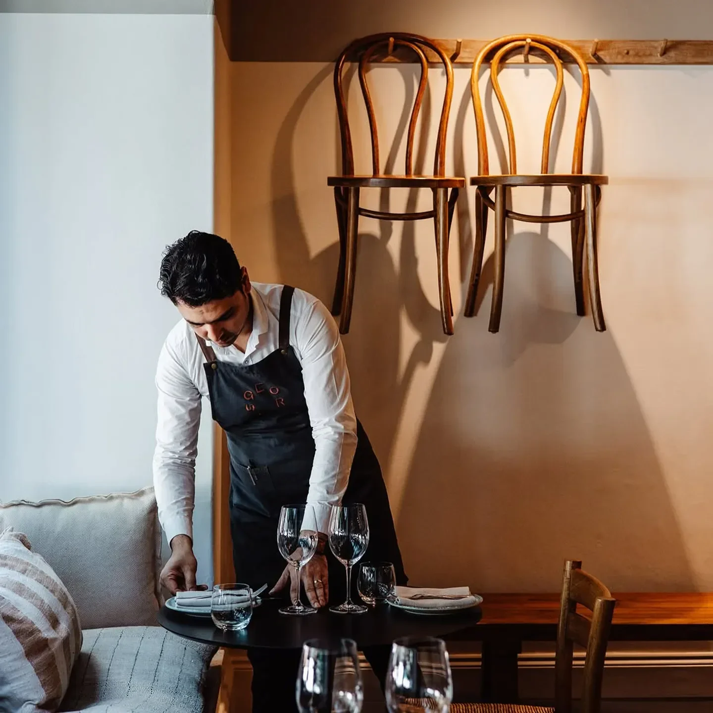 Server sets table at GEORGES restaurant in Adelaide, featuring hanging chairs and elegant decor.