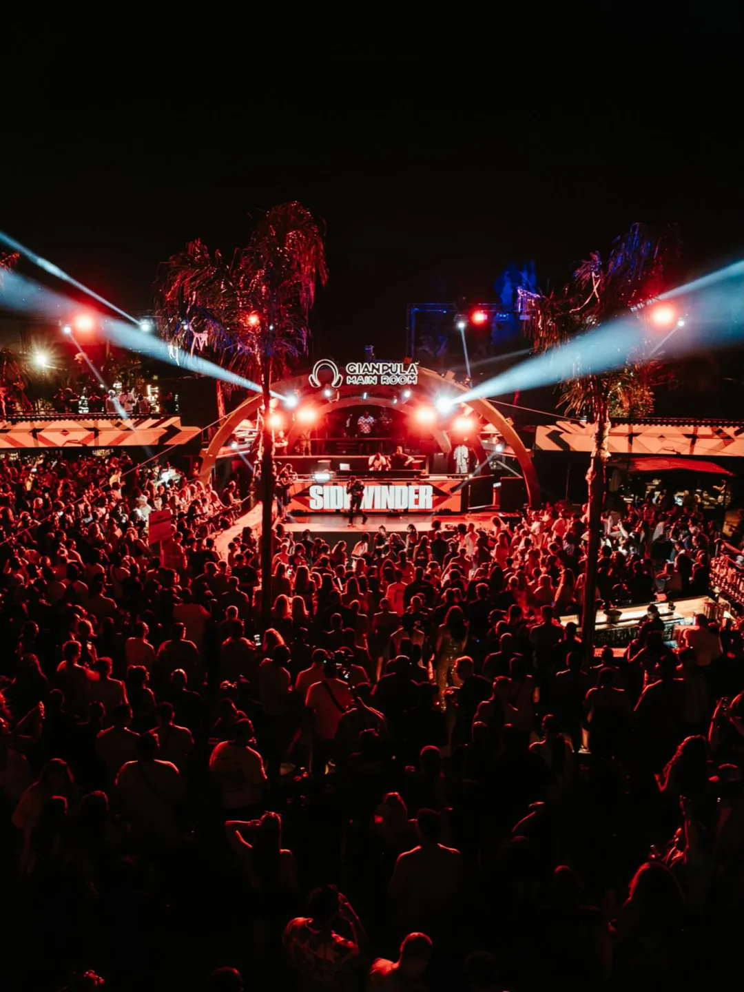 Crowded outdoor dance floor at Gianpula Village Malta with vibrant stage lights and palm trees.