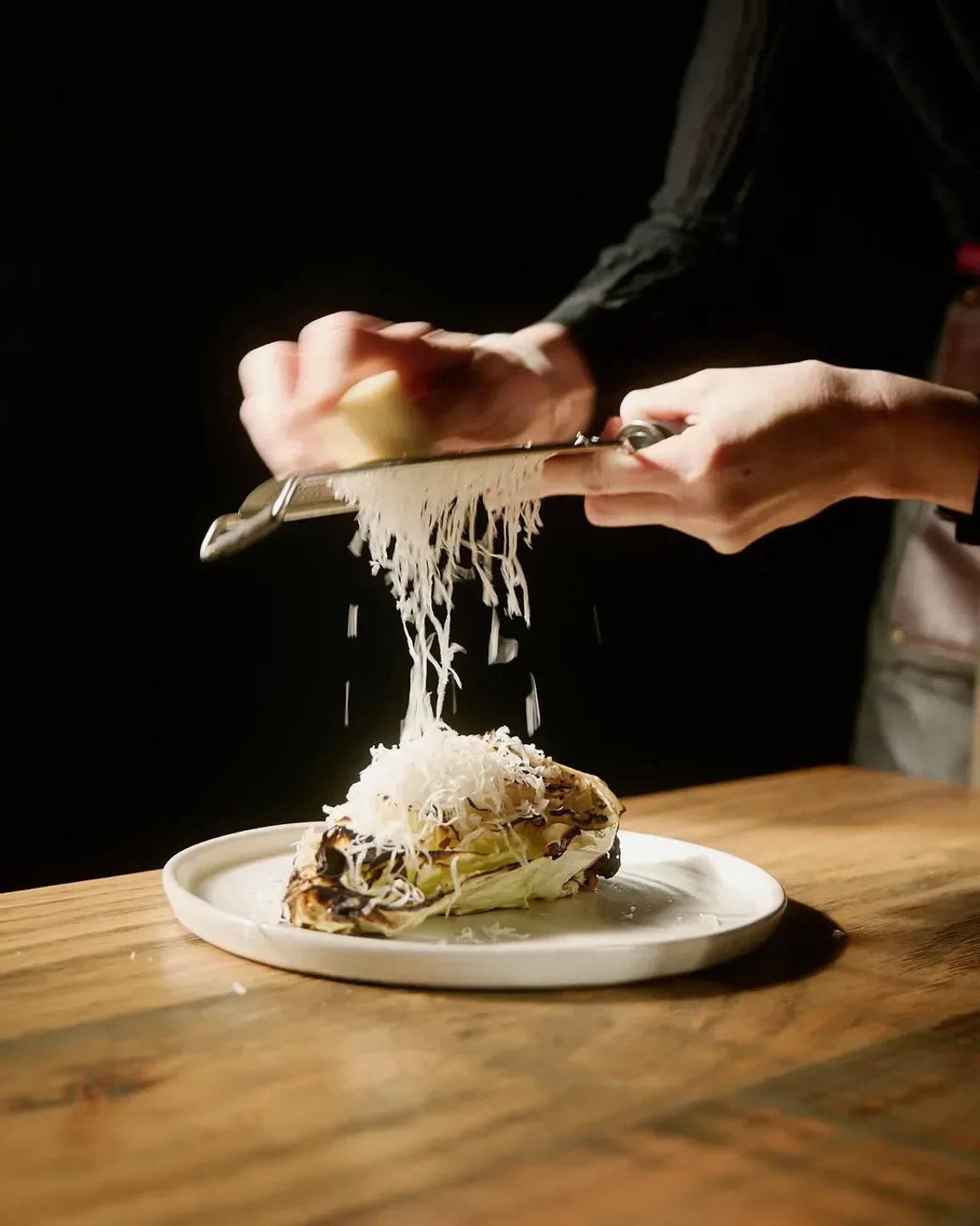 Chef grating cheese on a dish at Greasy Zoe's in Melbourne, adding the final touch.