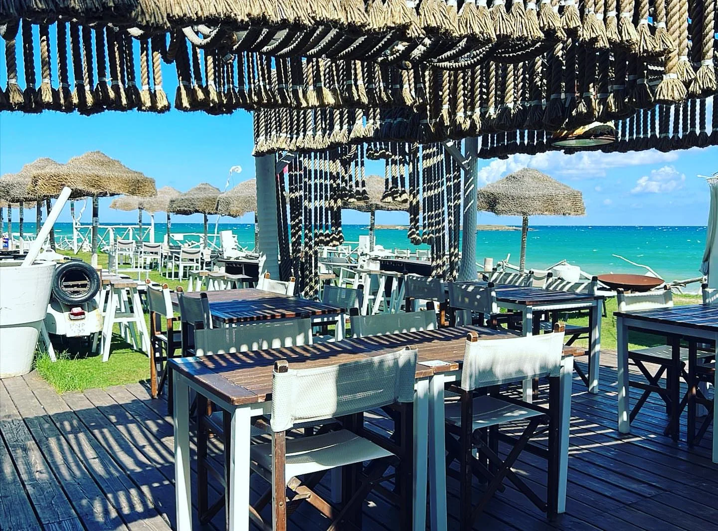 Outdoor seating at Guna Beach Club in Puglia with tables on wooden deck overlooking the turquoise sea.