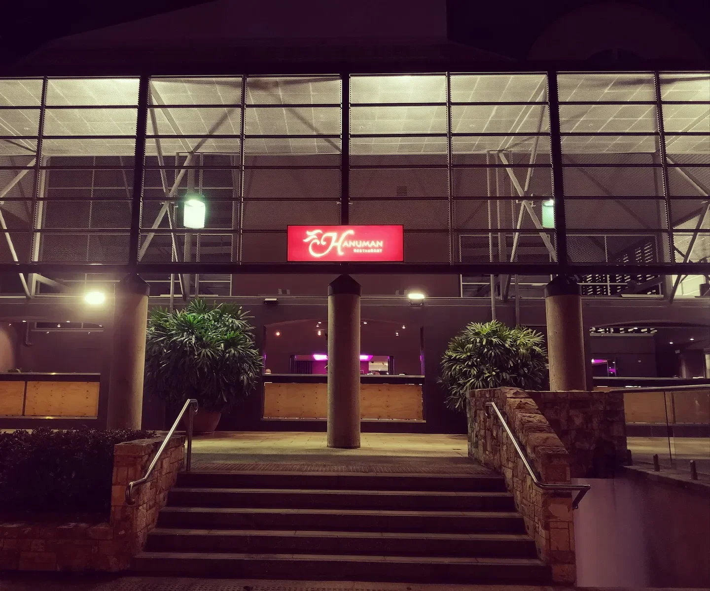 Entrance to Hanuman Restaurant in Darwin, featuring steps, pillars, and a glowing sign at night.