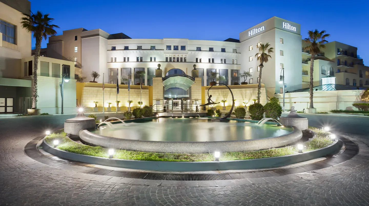 Hilton Malta hotel entrance with fountain, palm trees, and illuminated at dusk in Malta.