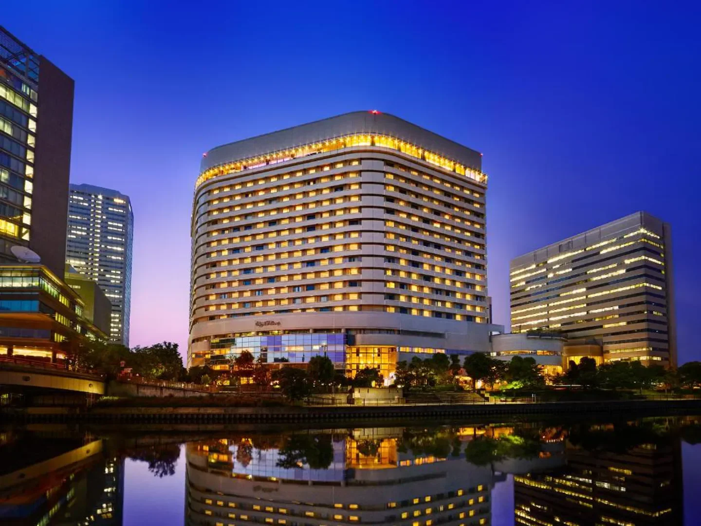 Hotel New Otani Osaka at dusk, with lights reflecting on the water in Osaka.