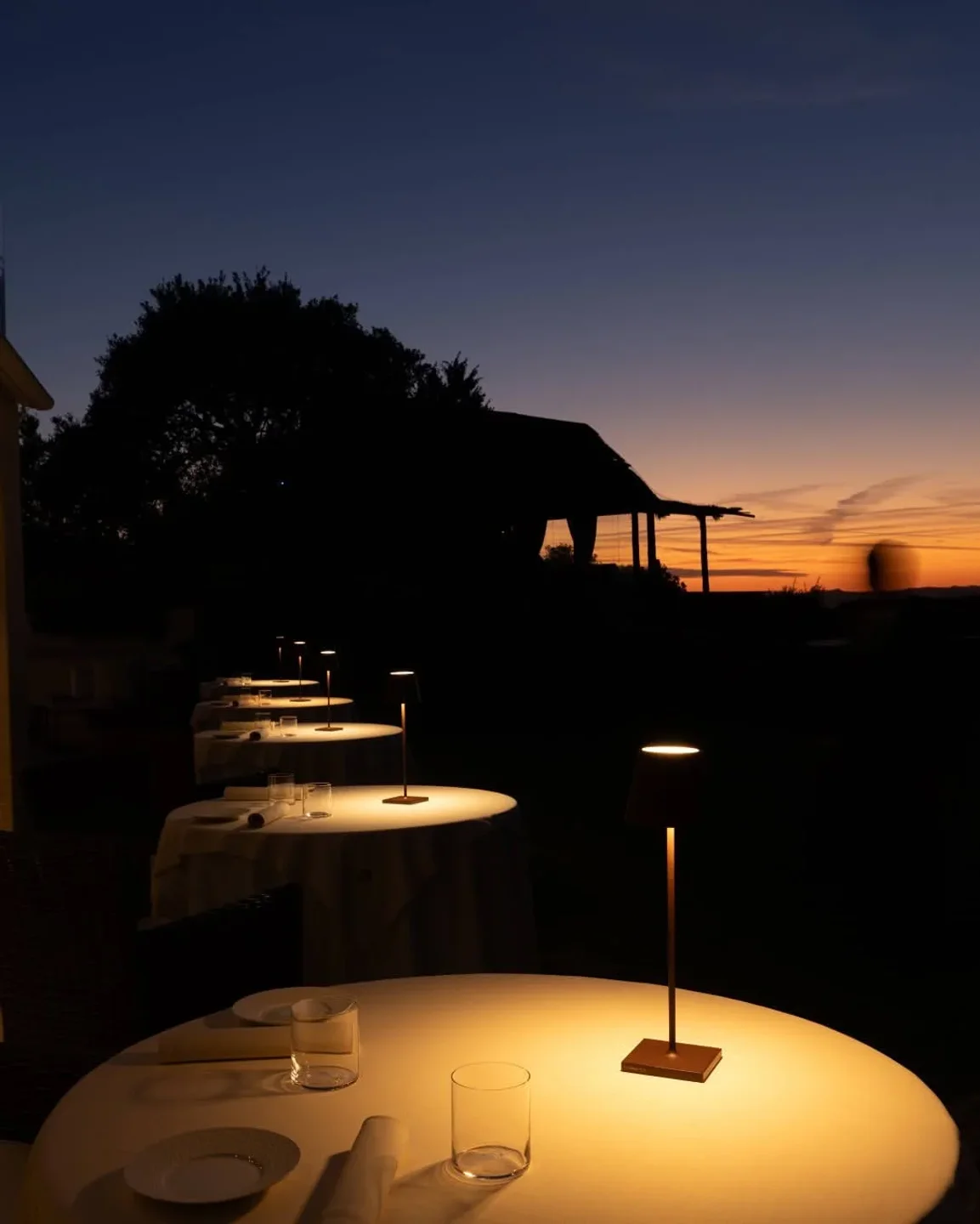 Outdoor dining ambiance at Il Fuoco Sacro in Sardinia with elegantly set tables under a twilight sky.