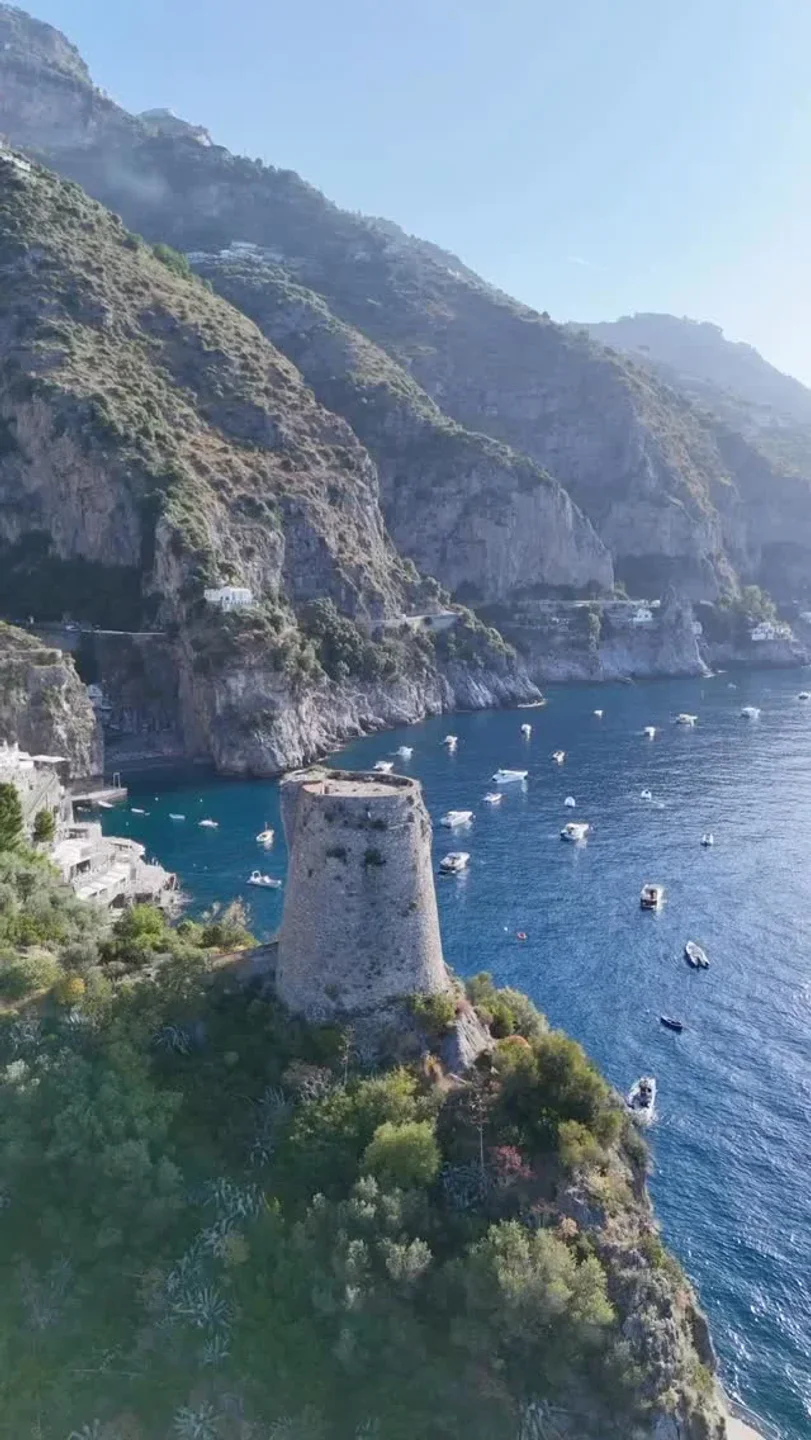 Il Pirata Praiano restaurant's historic tower overlooks boats in the stunning blue waters of Amalfi Coast.