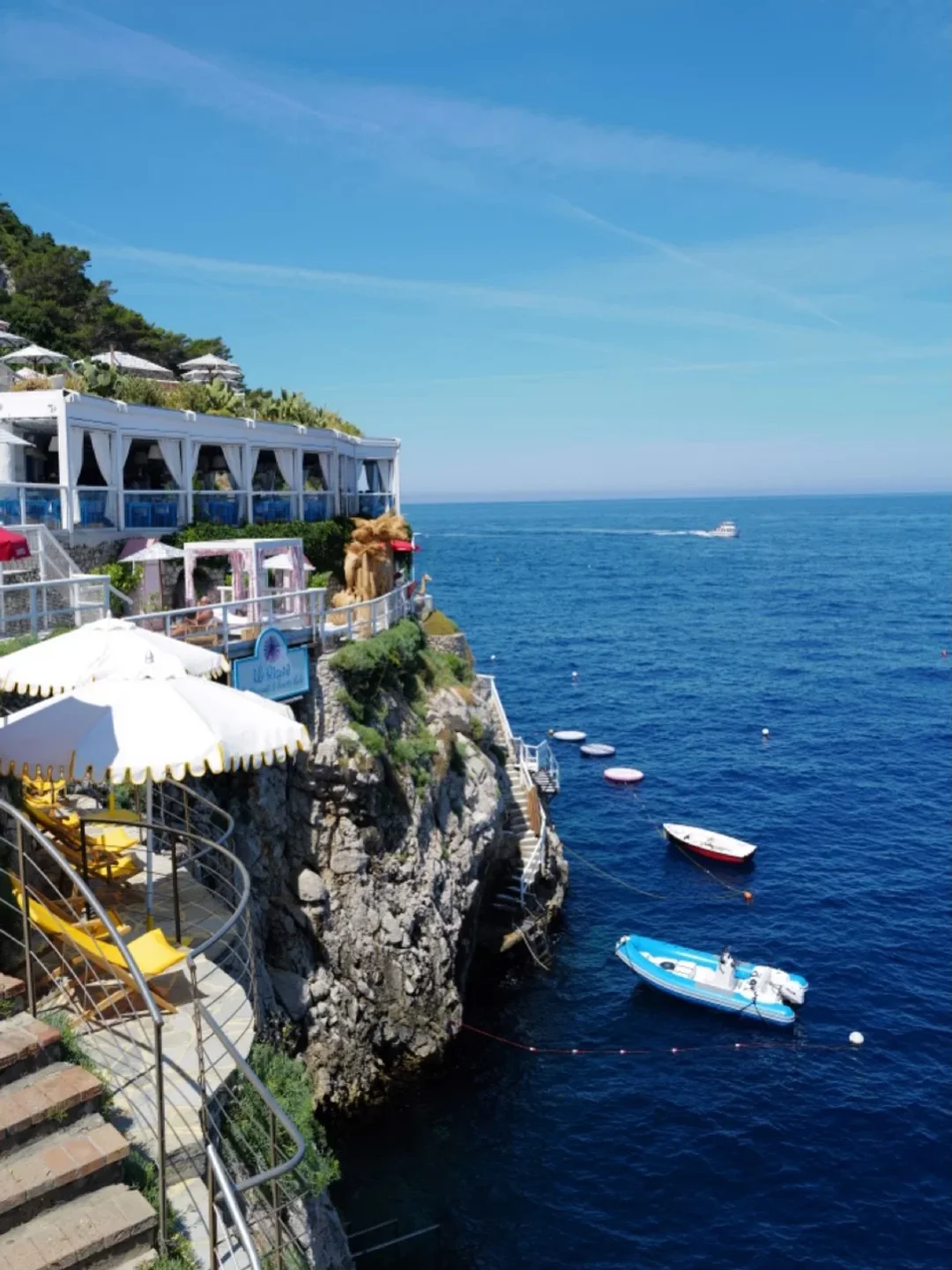 Il Riccio Restaurant & Beach Club in Capri perched on a cliff overlooking the turquoise sea with boats.
