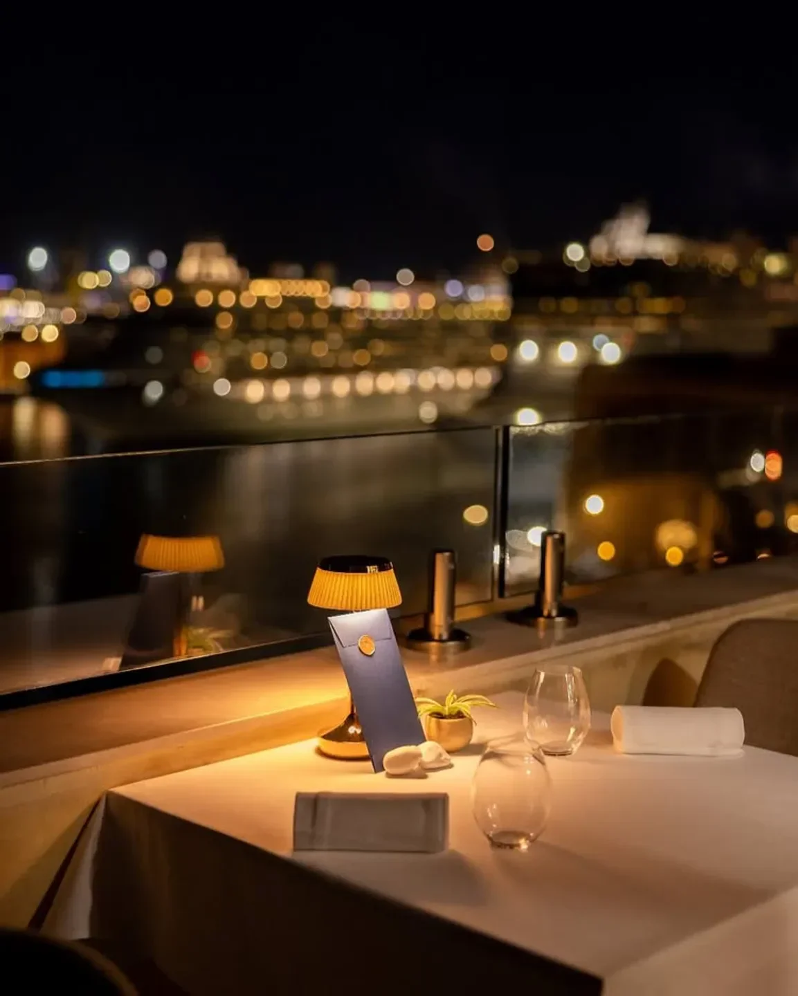 ION Harbour by Simon Rogan in Valletta at night, with a table set for dinner and city lights