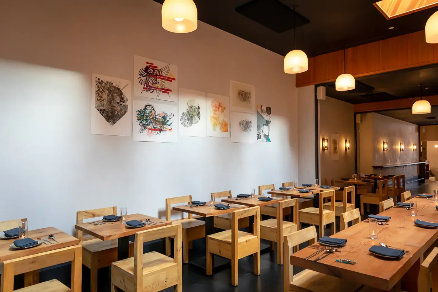 Interior dining space at Itria, a San Francisco restaurant with art and wooden tables.