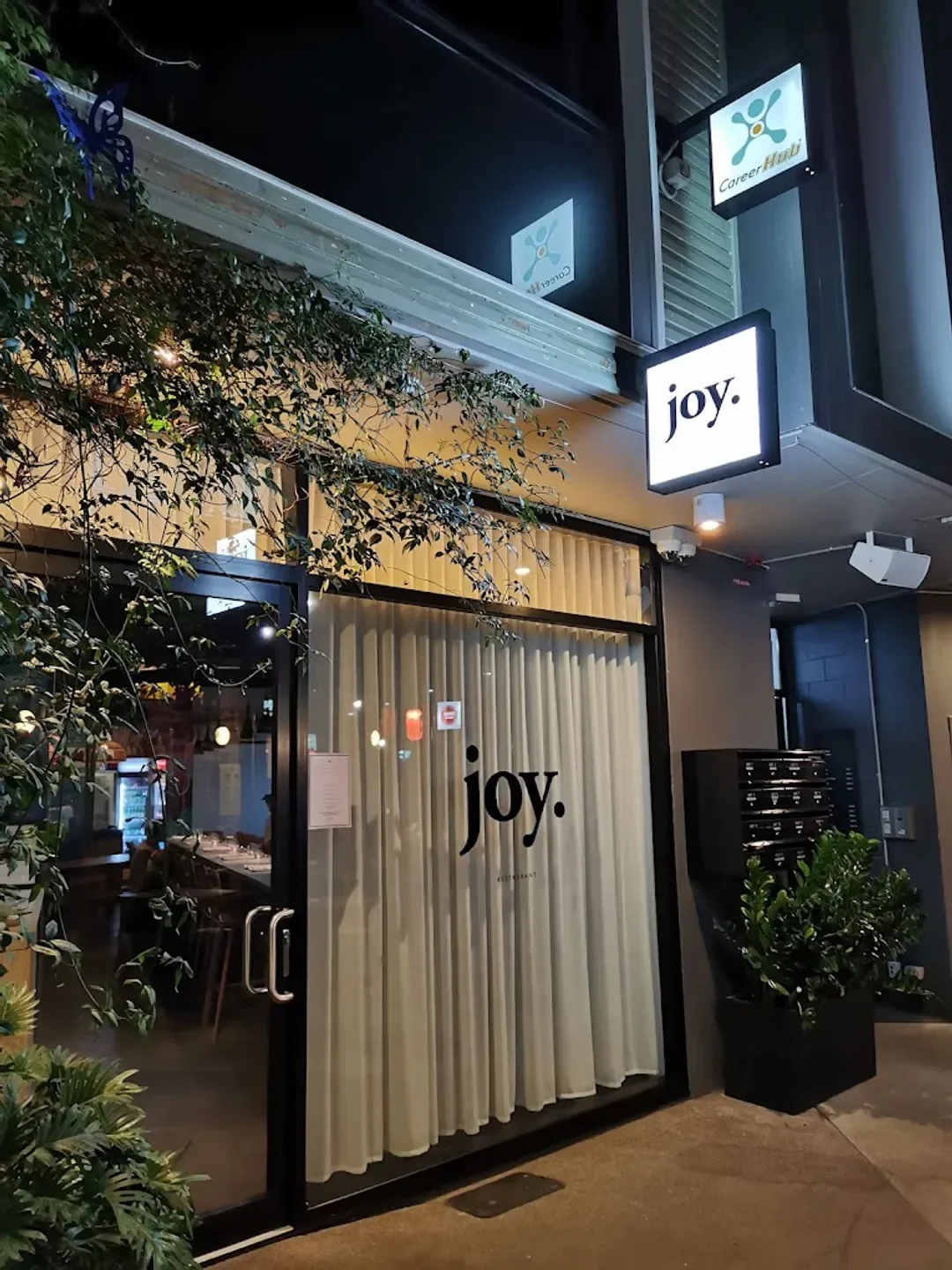Entrance to Joy restaurant in Brisbane, night exterior with illuminated sign and curtains.