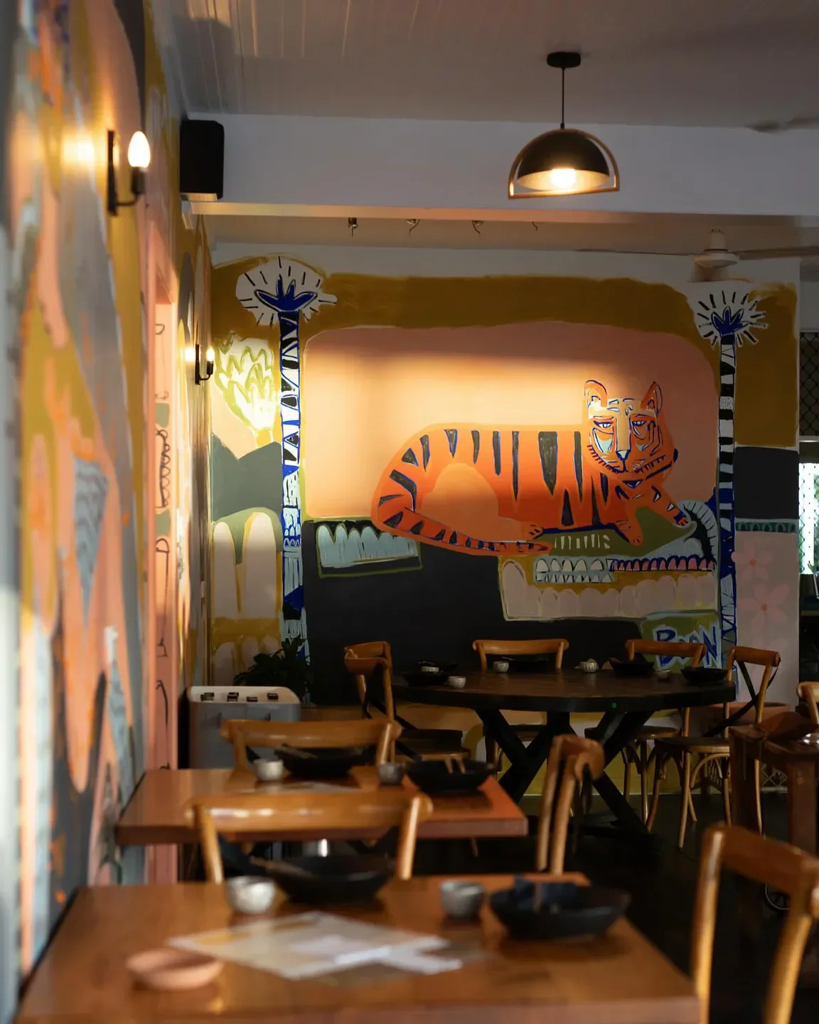 Interior of Jungle Fowl restaurant in Port Douglas featuring a tiger mural and wooden tables.