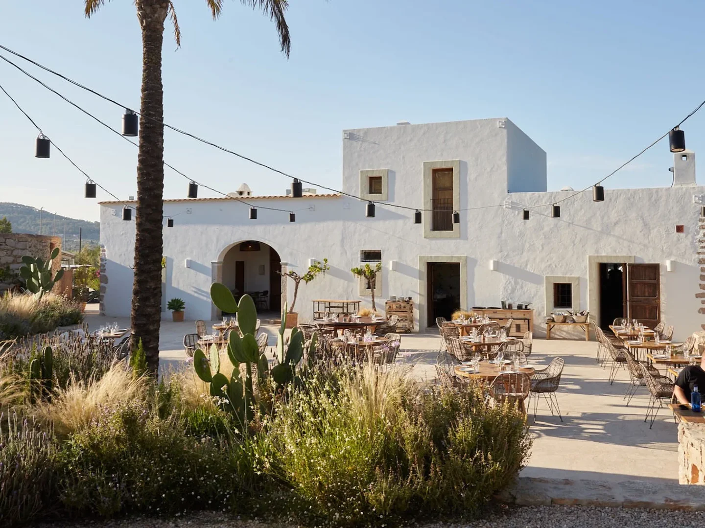 Juntos House Ibiza restaurant patio with rustic tables, string lights, and lush Mediterranean landscaping.