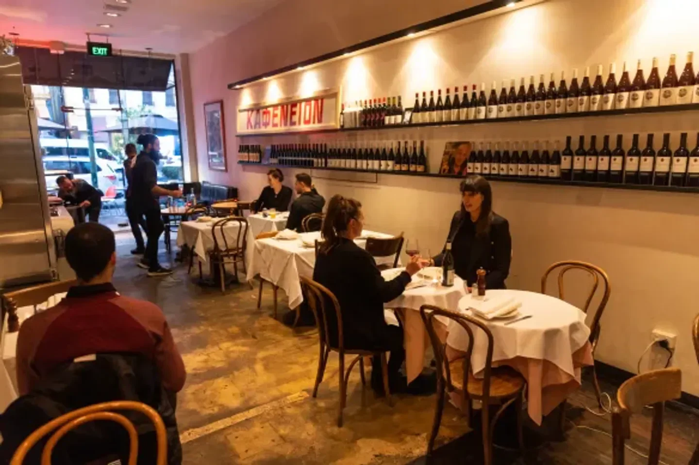 Interior dining scene at Kafeneion restaurant in Melbourne, with tables and wine bottles.