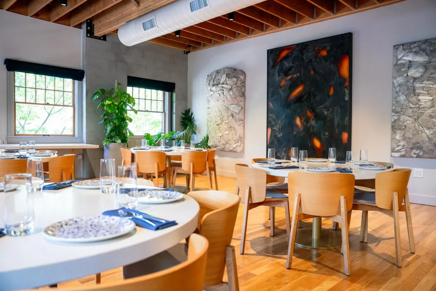 Interior dining space at Kann restaurant in Portland, featuring art, wooden chairs, and elegant table settings.