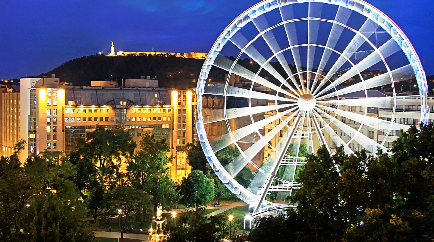 Ferris wheel and Kempinski Hotel Corvinus Budapest illuminated at night in Budapest.