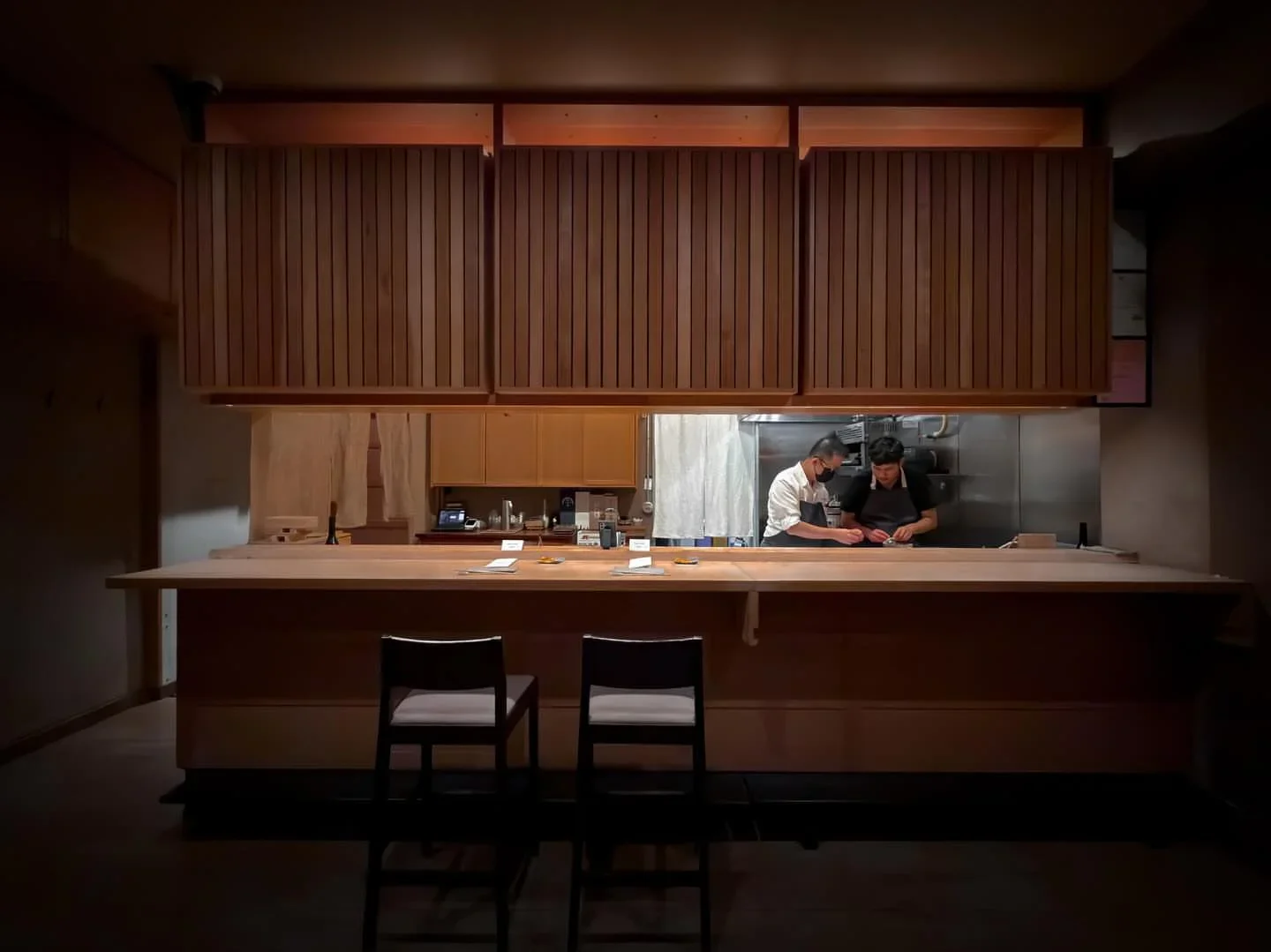 Interior view of the bar and kitchen at KEN restaurant in San Francisco, featuring chefs preparing food.