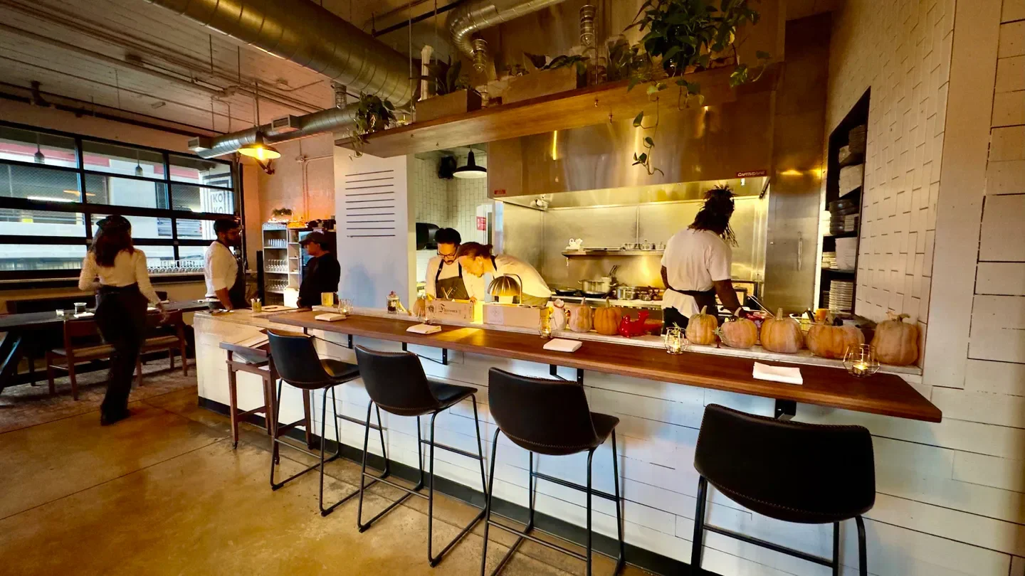 Interior of Koko Ni in Denver: bar seating with chefs preparing food, pumpkins on display.