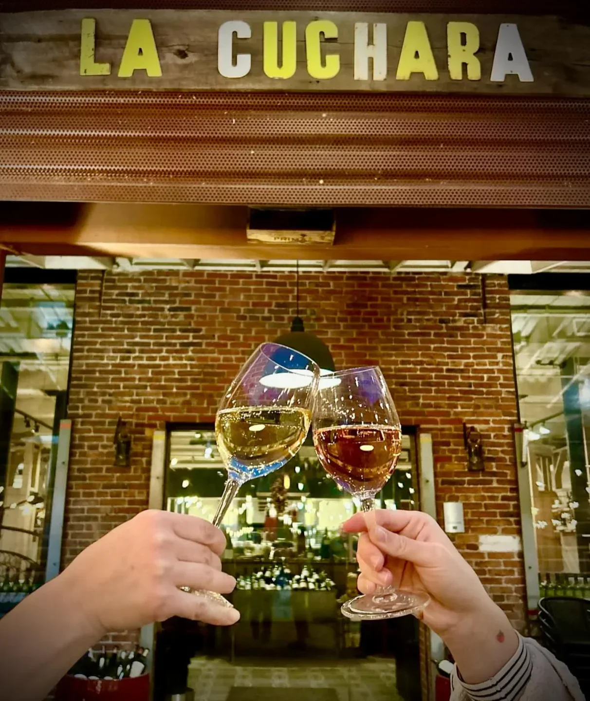 Cheers at La Cuchara in Baltimore. Wine glasses clink in front of the restaurant interior.