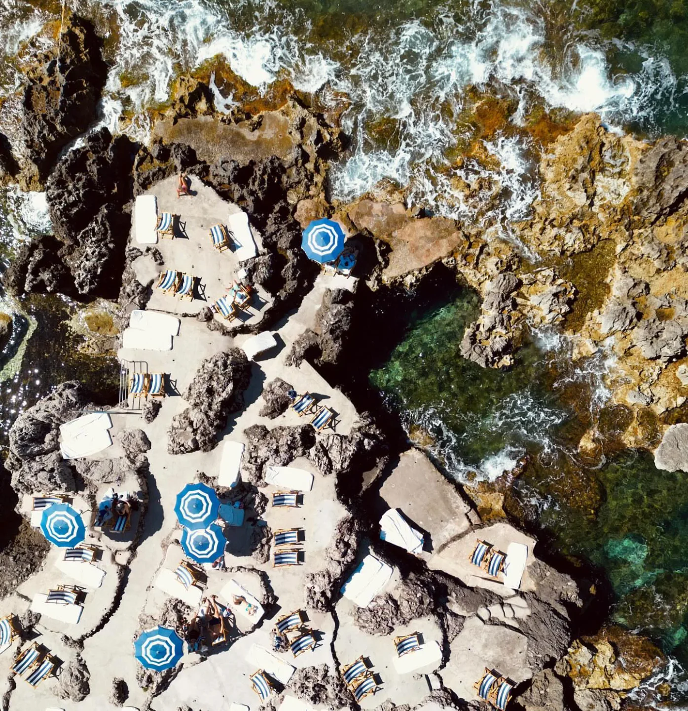 Aerial view of La Fontelina beach club in Capri with striped loungers and blue umbrellas by the sea