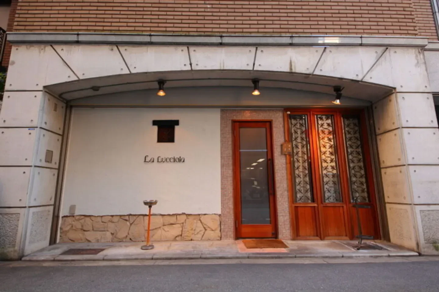 Entrance of La Lucciola restaurant in Osaka, with wooden doors and stylish architecture.