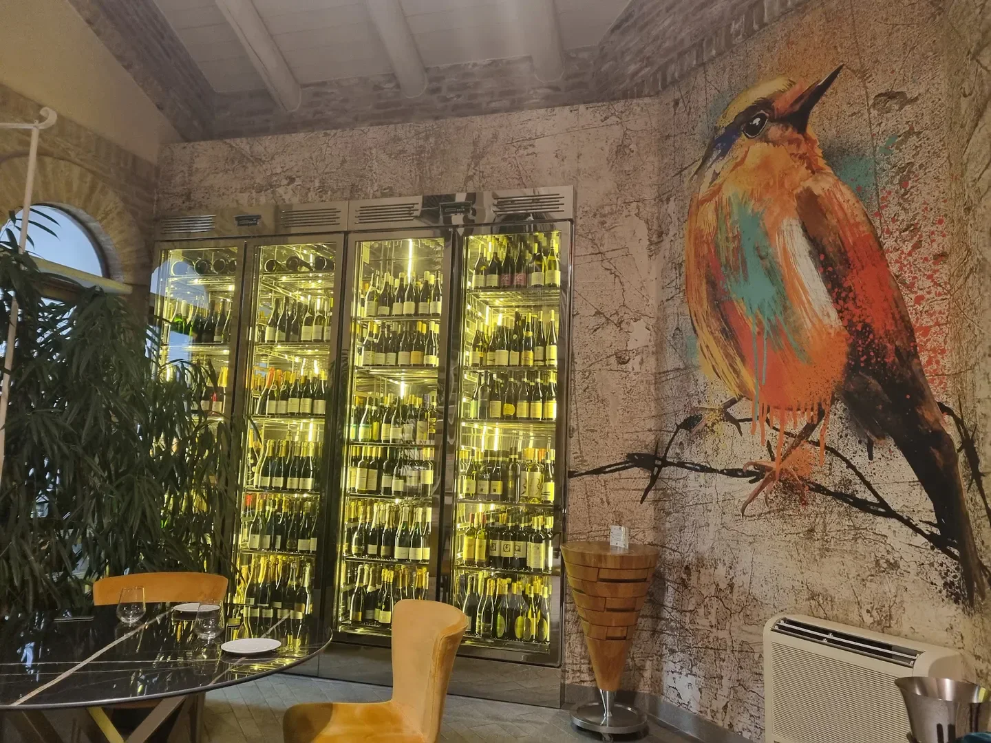 Interior of La Madernassa restaurant in Langhe, featuring wine selection and a colorful bird mural.