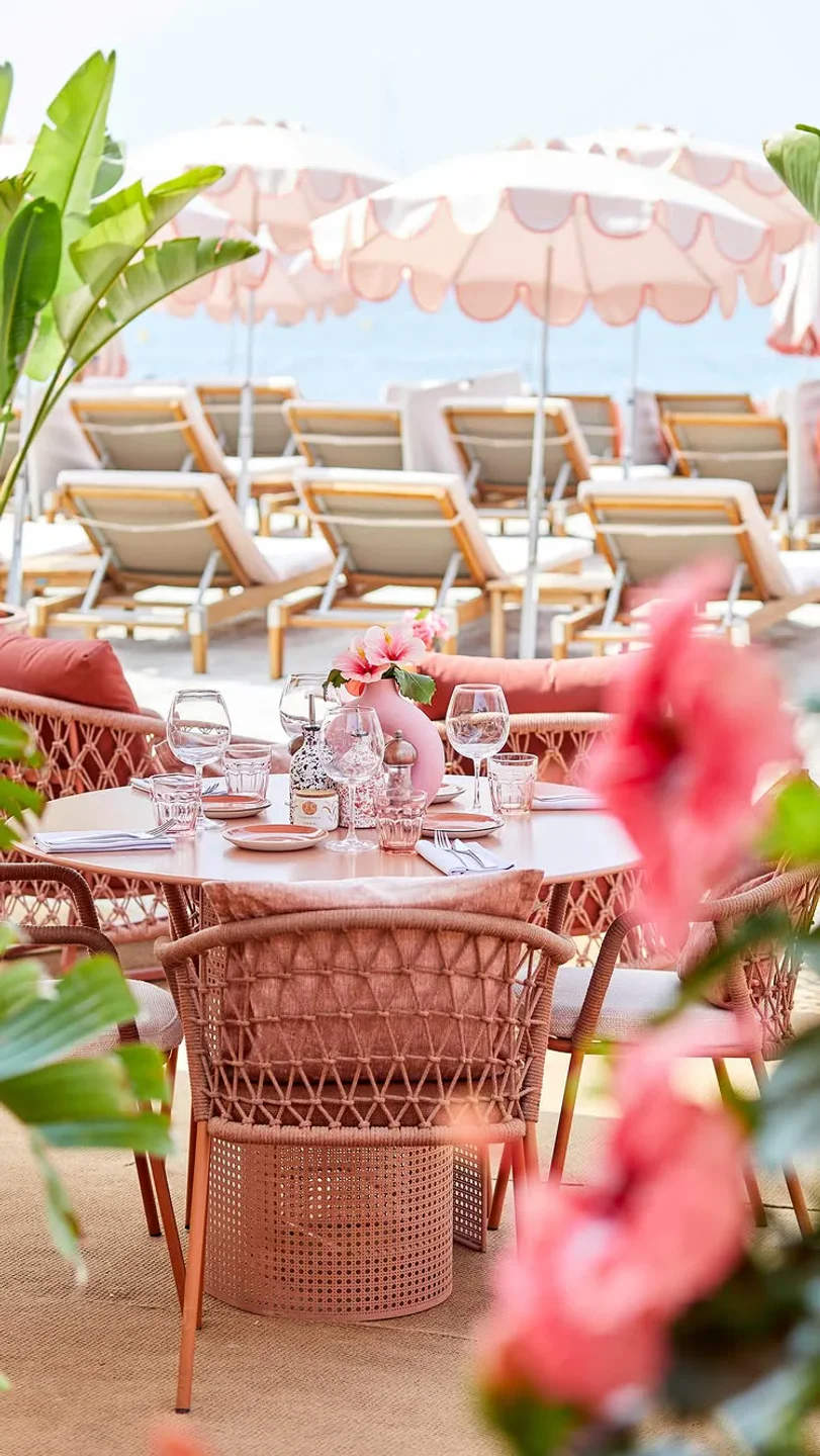 Chic outdoor seating at La Mandala restaurant overlooking the beach in the city, with pink umbrellas and lounge chairs.