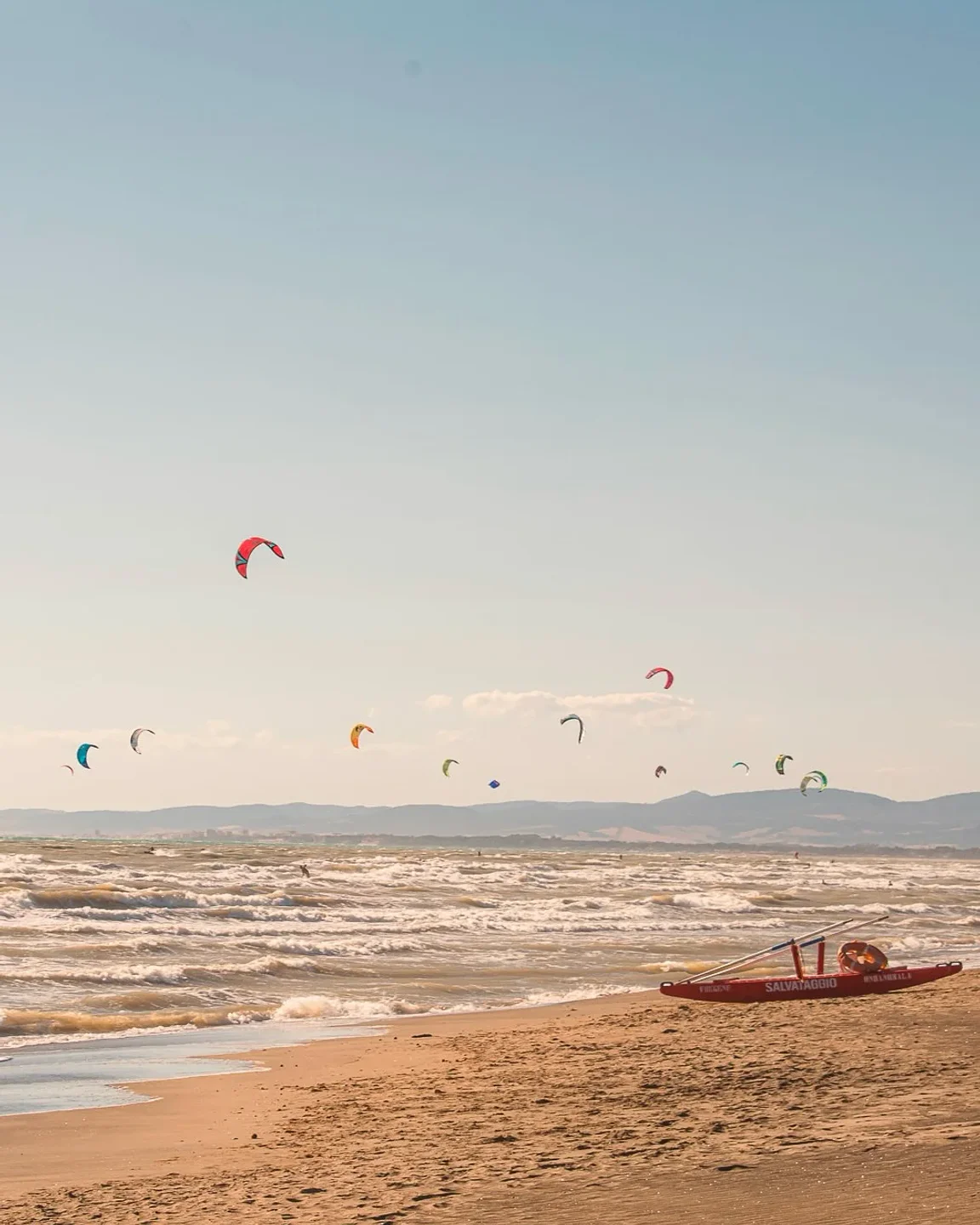 Kite surfers enjoy windy conditions at La Scialuppa da Salvatore beach club with lifeguard boat on shore.