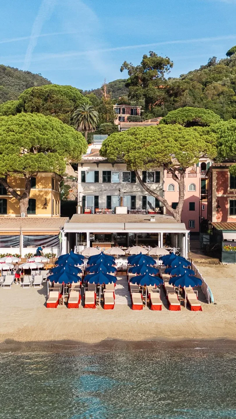 La Scogliera Paraggi beach club with red lounge chairs and blue umbrellas on Italian Riviera sandy shore