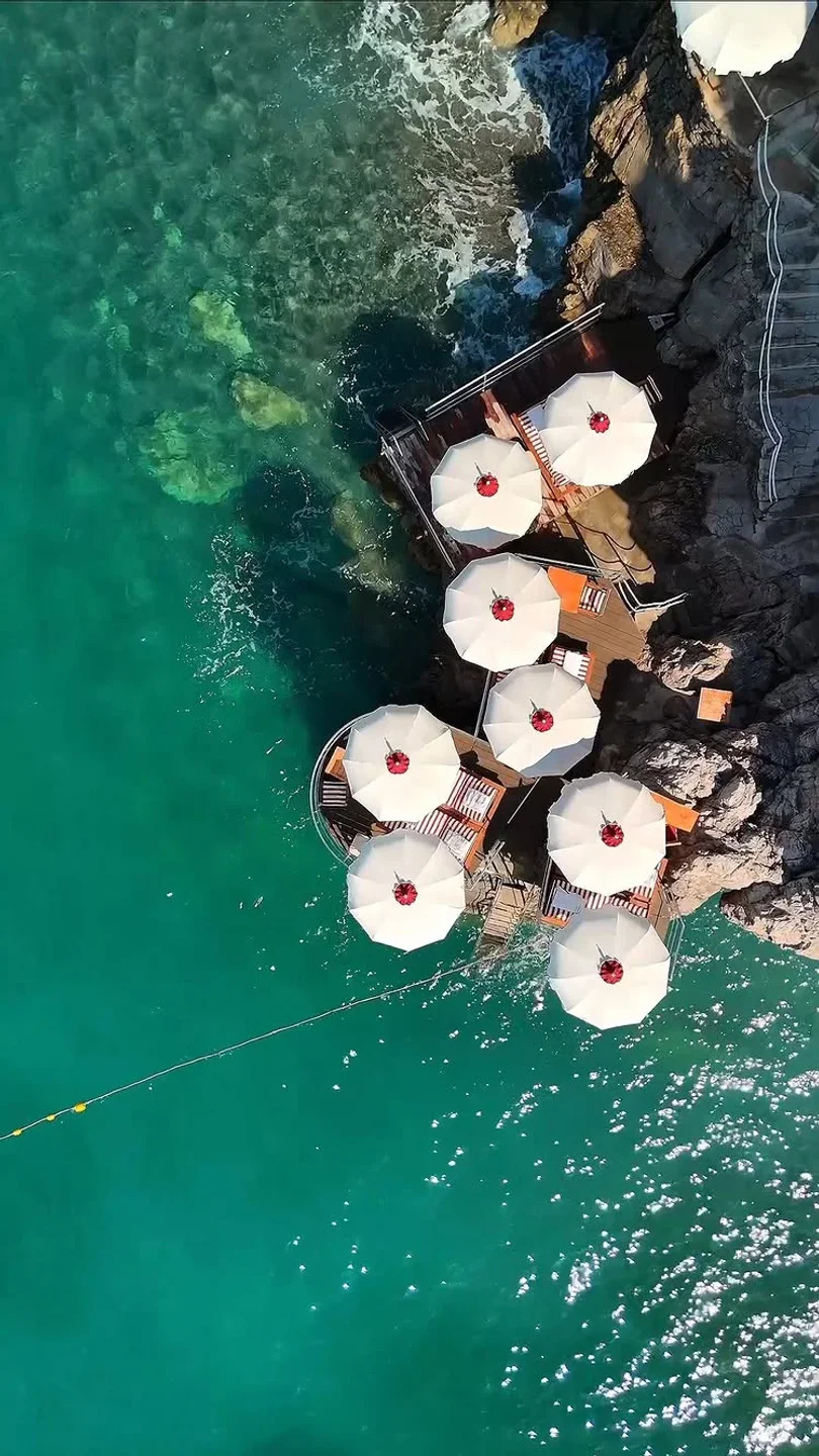 Aerial view of La Scogliera Positano beach club with white umbrellas and turquoise waters on the Amalfi Coast