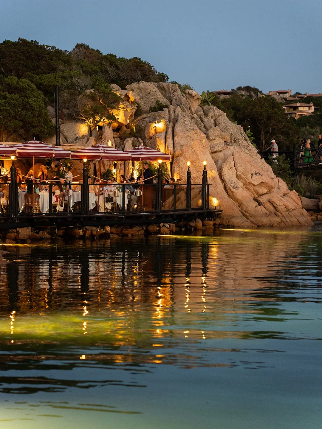 Langosteria restaurant in Porto Cervo with illuminated waterfront dining and rocky coastal backdrop at dusk.
