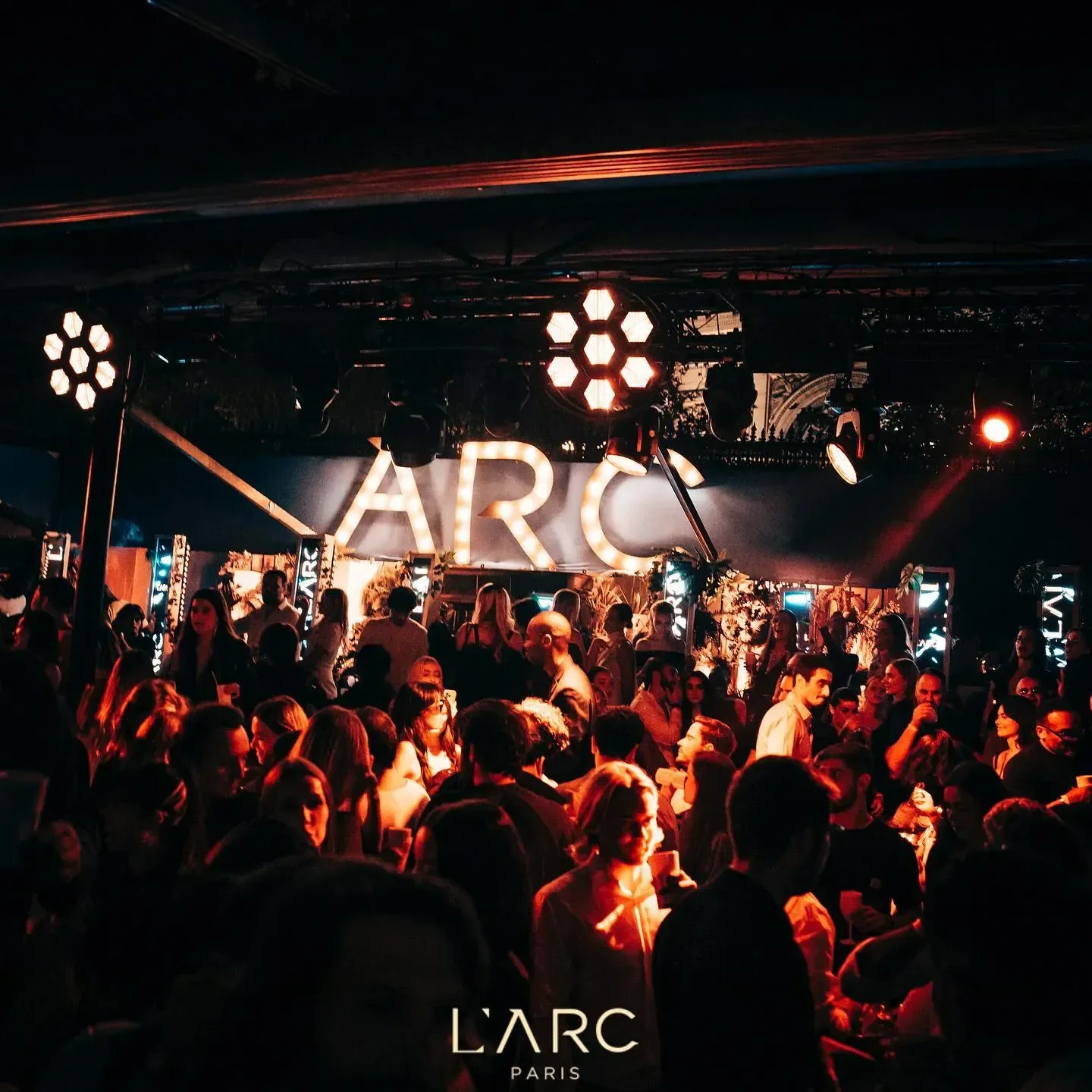 Energetic crowd partying at L'Arc nightclub in Paris, illuminated with vibrant lights.