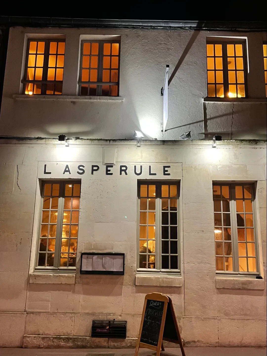 Exterior of L'Aspérule restaurant in Bourgogne, illuminated at night with inviting windows.