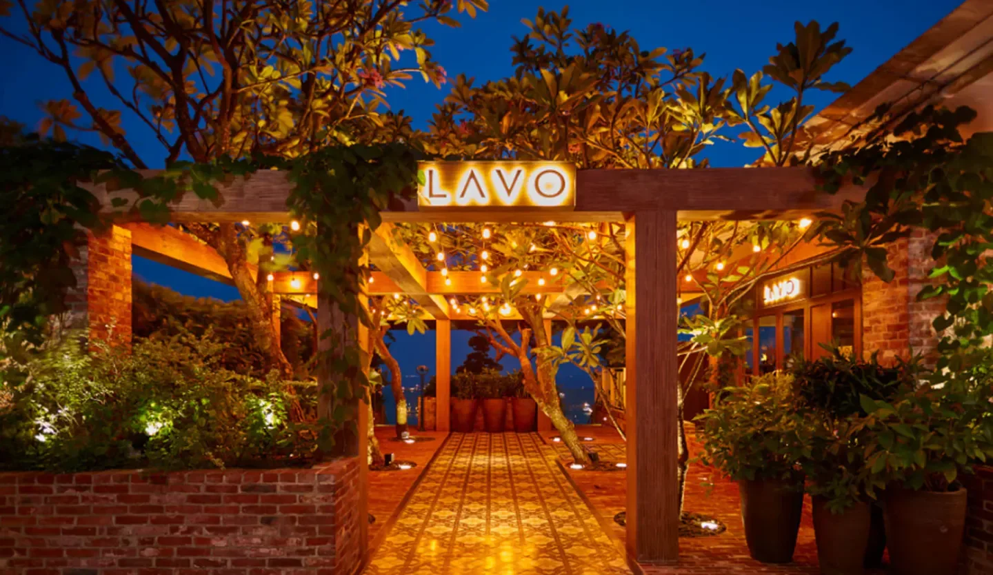Entrance to LAVO Singapore, featuring wooden beams, string lights, and lush greenery at dusk.