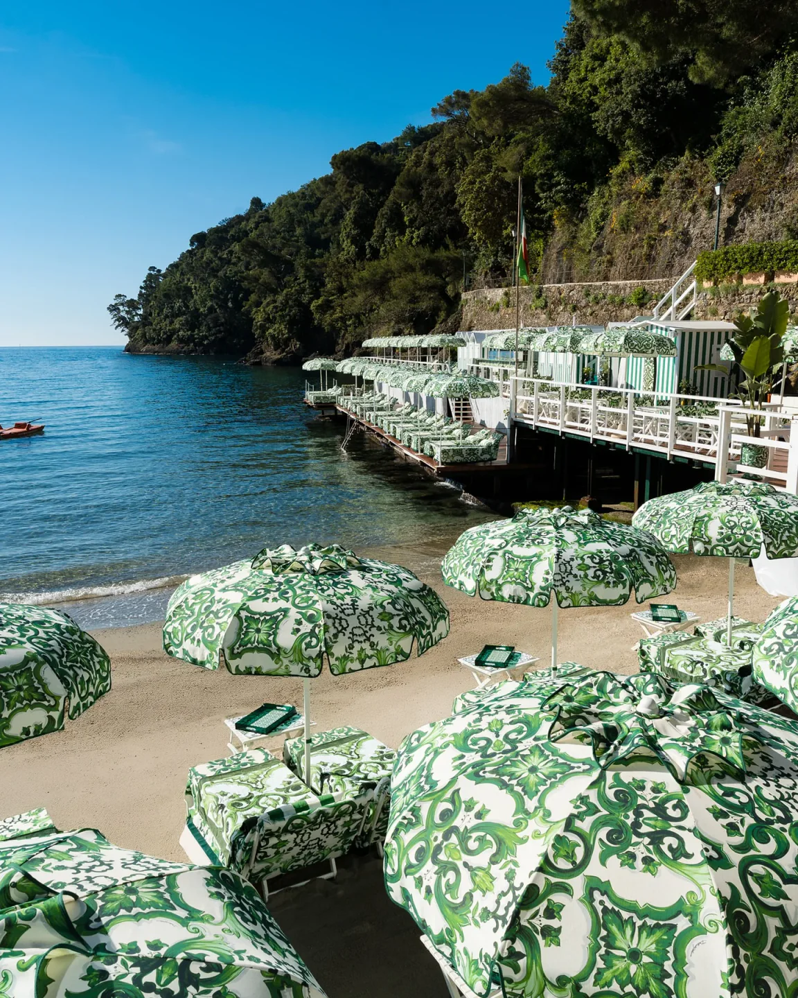 Le Carillon Portofino beach club loungers and umbrellas on Italian Riviera sandy shore with clear blue water.