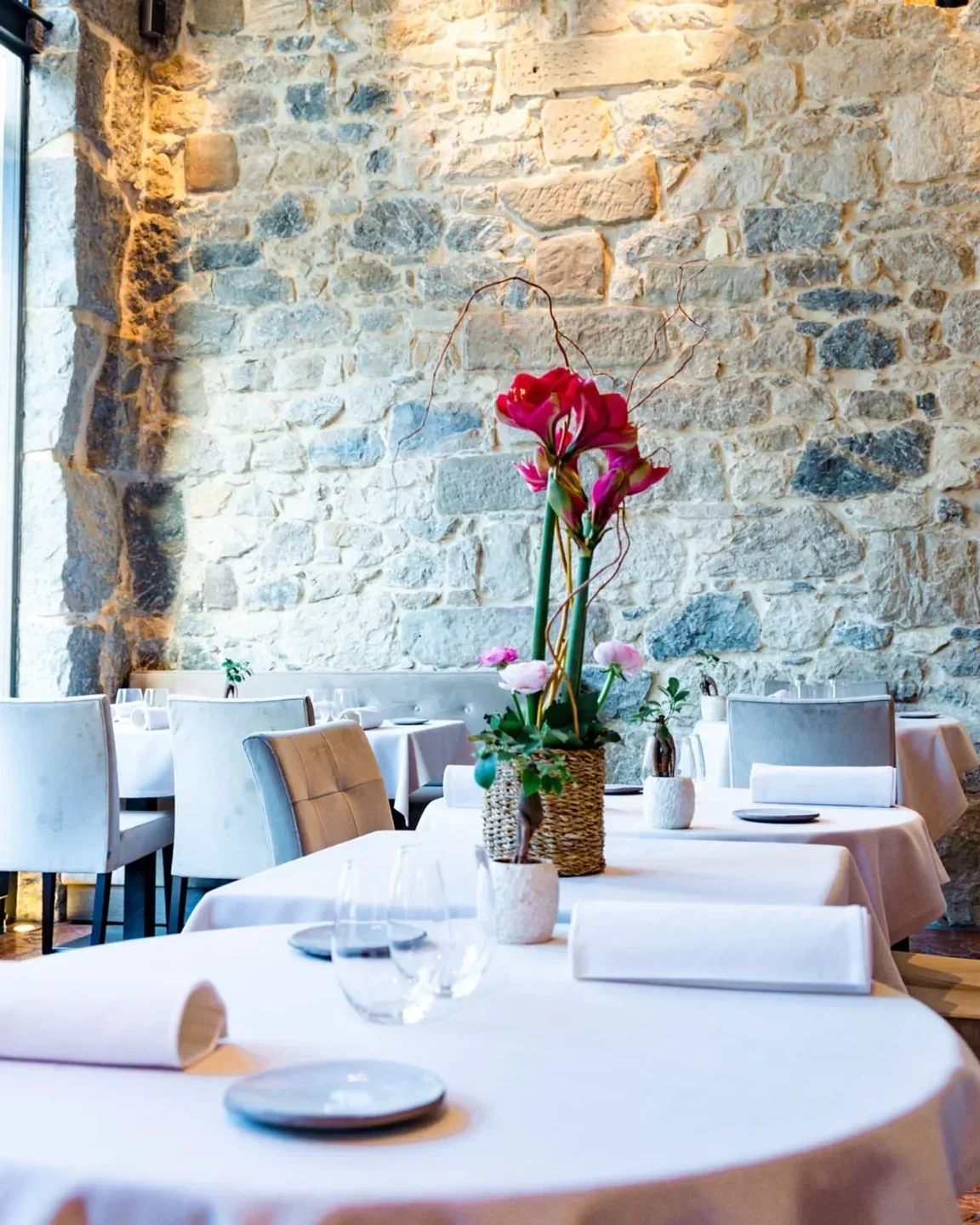 Elegant dining at Le Flacon restaurant in Geneva, with stone wall and floral centerpiece.