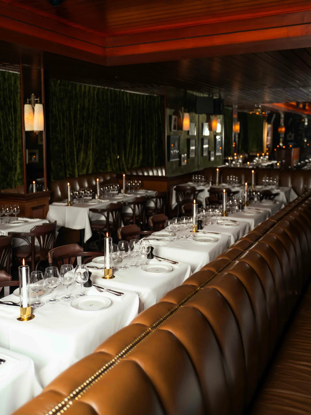 Elegant dimly lit dining room interior at Le Pompon restaurant with candlelit tables and leather banquettes.