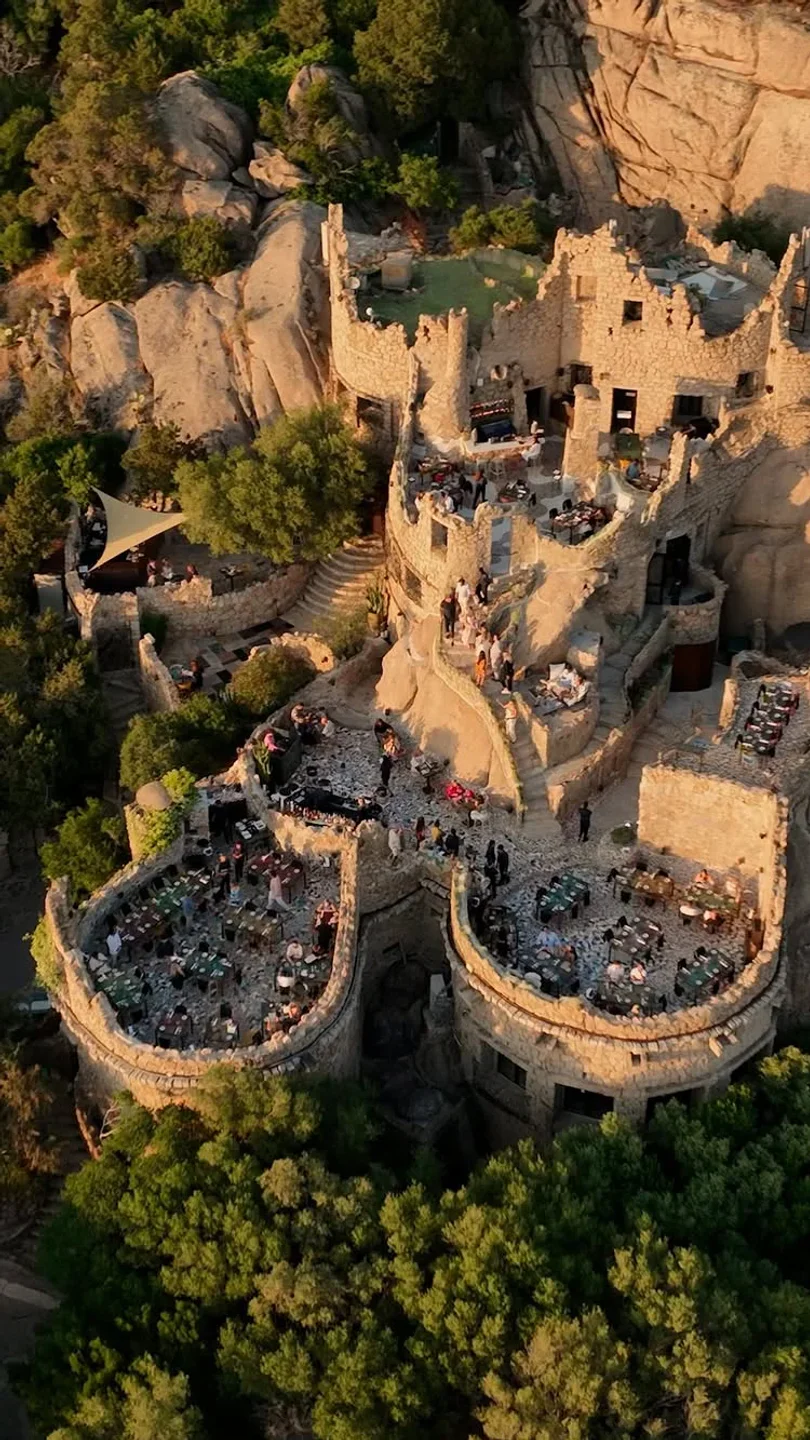 Le Terrazze Ritual restaurant exterior in Porto Cervo, built into a rocky hillside overlooking trees.