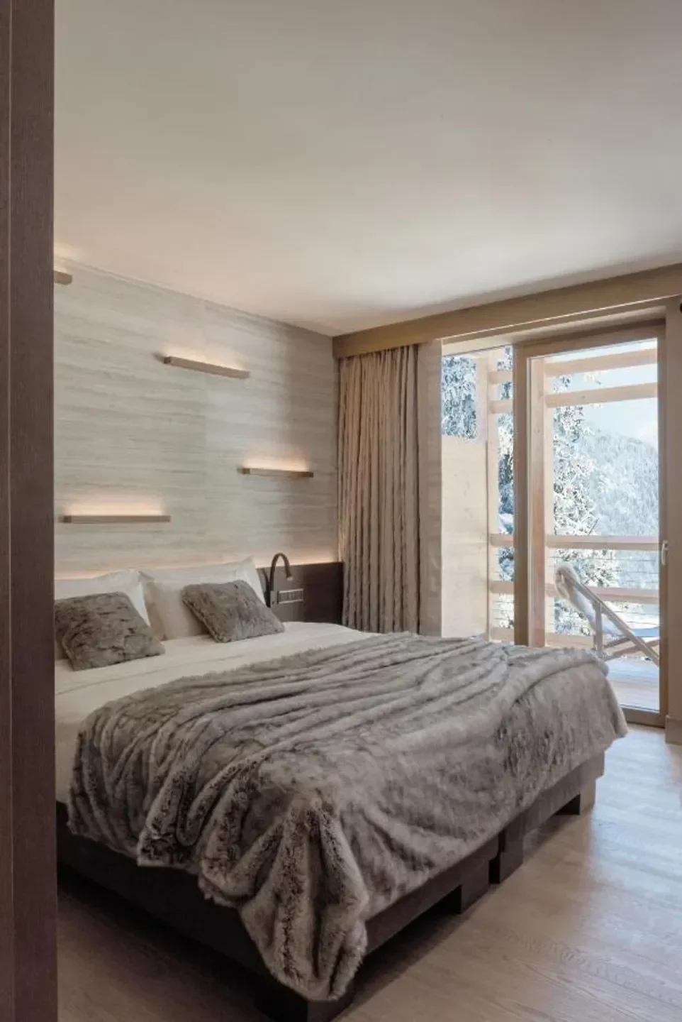 Cozy bedroom at Lefay Resort & SPA Dolomiti in Milan, with a view of snow-covered mountains.