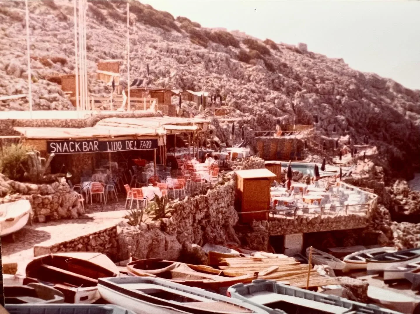 Lido del Faro beach club in Capri with rocky cliffs, snack bar, and boats on shore.